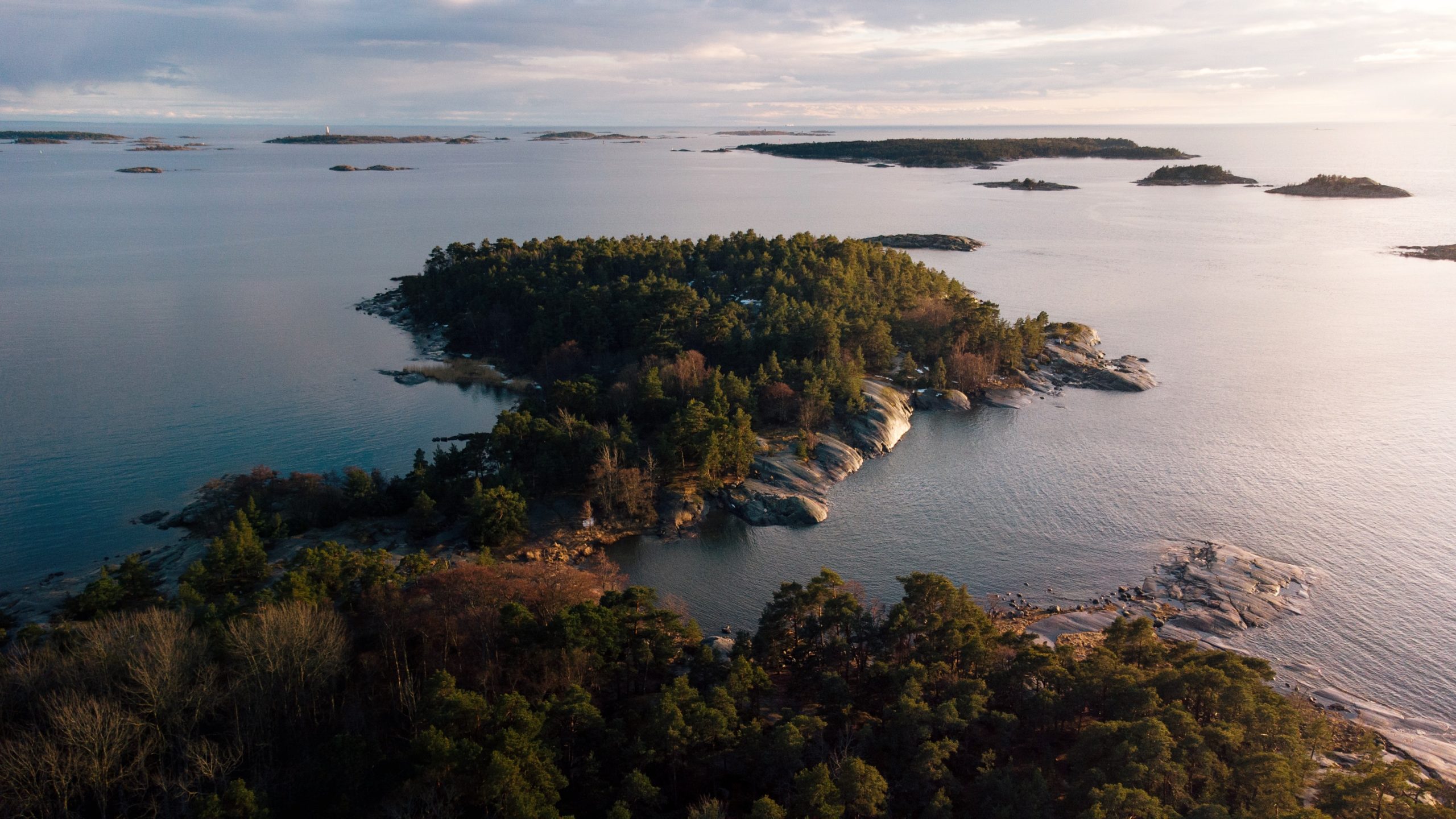 Ilmakuva saarimaisemasta. Tasainen vedenpinta ja paljon metsää ja kallioita.